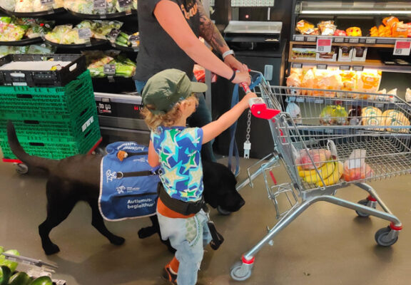 Ein Autismusbegleithund begleitet Kind und Mutter beim Einkaufen